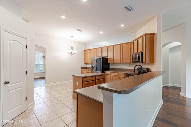 kitchen with light hardwood / wood-style flooring, appliances with stainless steel finishes, hanging light fixtures, kitchen peninsula, and a center island