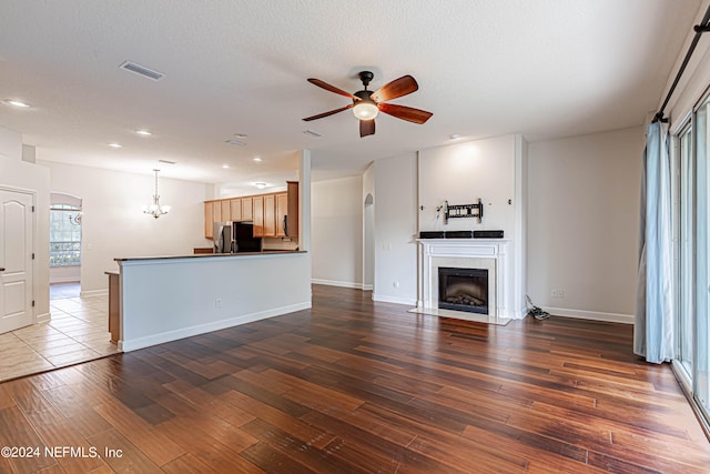 unfurnished living room with a textured ceiling, dark wood-type flooring, ceiling fan with notable chandelier, and a tile fireplace