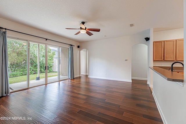 unfurnished living room with dark wood-type flooring, a textured ceiling, sink, and ceiling fan