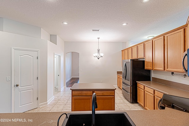 kitchen featuring a textured ceiling, a kitchen island, sink, hanging light fixtures, and stainless steel refrigerator with ice dispenser