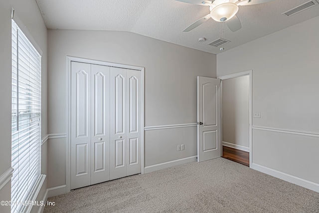 unfurnished bedroom featuring lofted ceiling, a closet, carpet floors, ceiling fan, and a textured ceiling