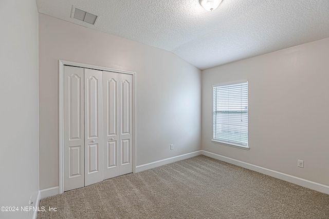 unfurnished bedroom featuring carpet, a textured ceiling, lofted ceiling, and a closet