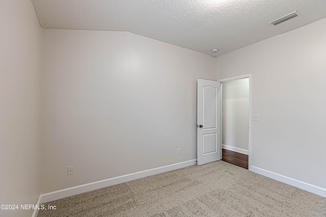 empty room with a textured ceiling, vaulted ceiling, and carpet floors