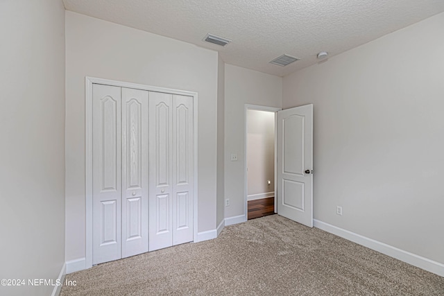 unfurnished bedroom with a textured ceiling, carpet floors, and a closet