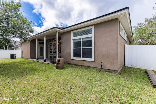 rear view of property featuring cooling unit, a lawn, and a patio area