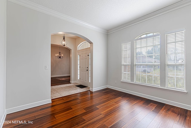 entrance foyer featuring a textured ceiling, ornamental molding, wood-type flooring, and a chandelier