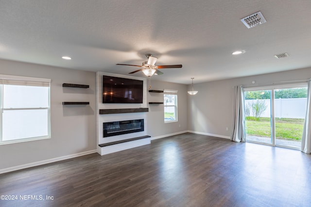 unfurnished living room featuring a textured ceiling, a large fireplace, ceiling fan, and dark hardwood / wood-style floors