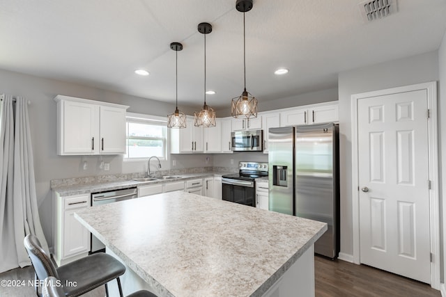 kitchen with white cabinets, appliances with stainless steel finishes, sink, dark hardwood / wood-style floors, and pendant lighting