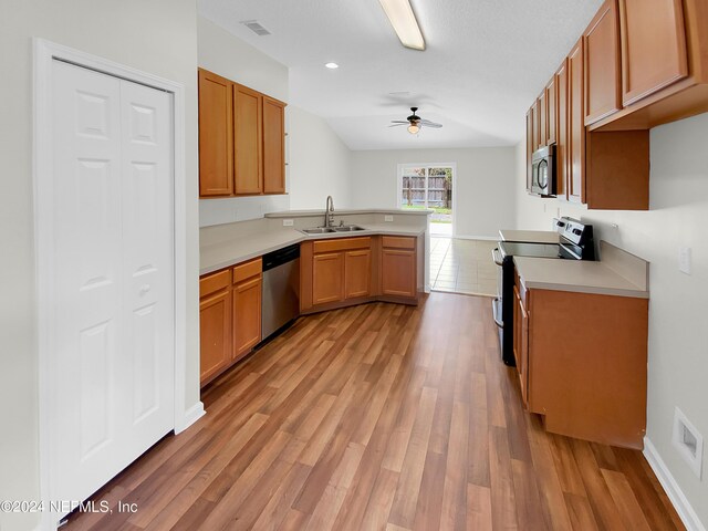 kitchen featuring appliances with stainless steel finishes, sink, light wood-type flooring, kitchen peninsula, and ceiling fan