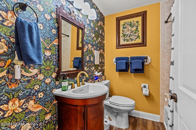 full bath with toilet, a textured ceiling, wood finished floors, baseboards, and vanity