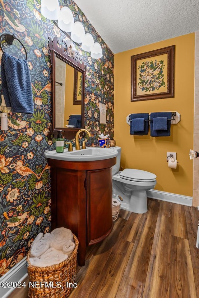 bathroom with toilet, a textured ceiling, wood finished floors, baseboards, and vanity