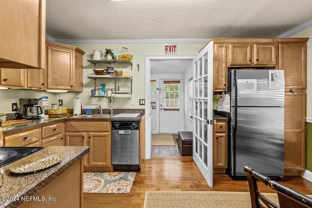 kitchen featuring dark countertops, a sink, appliances with stainless steel finishes, crown molding, and light wood-type flooring