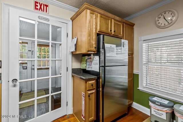 kitchen with crown molding, hardwood / wood-style floors, stainless steel fridge, dark stone counters, and a textured ceiling