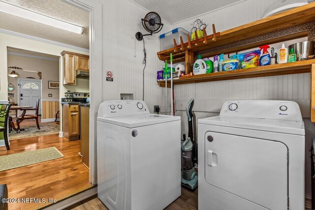 washroom with a textured ceiling, wood walls, light hardwood / wood-style flooring, washing machine and clothes dryer, and ornamental molding