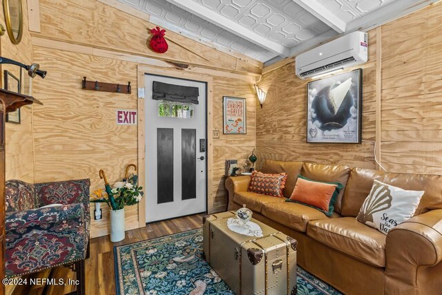 living room featuring wood-type flooring, an AC wall unit, a barn door, wooden walls, and vaulted ceiling with beams