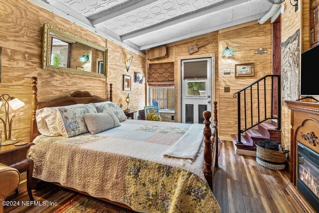 bedroom with lofted ceiling with beams, dark wood-type flooring, and wooden walls