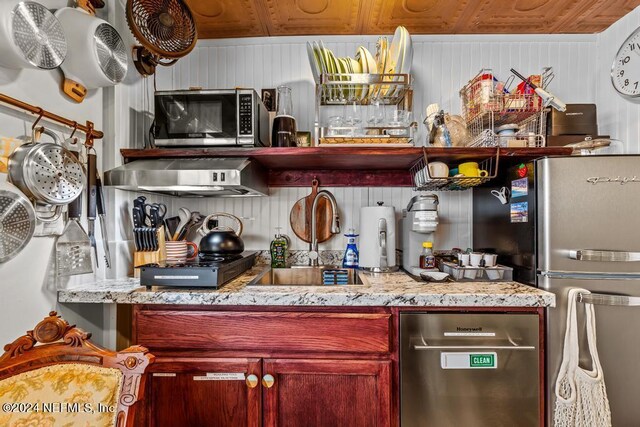 kitchen featuring wooden walls, light stone counters, sink, wooden ceiling, and appliances with stainless steel finishes