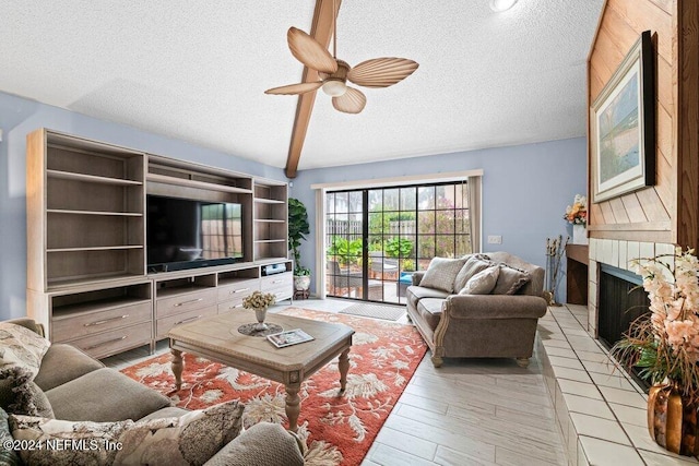 living room featuring a tiled fireplace, ceiling fan, light hardwood / wood-style floors, and a textured ceiling