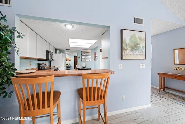 kitchen featuring white cabinetry, stainless steel range with electric cooktop, a kitchen bar, kitchen peninsula, and a textured ceiling