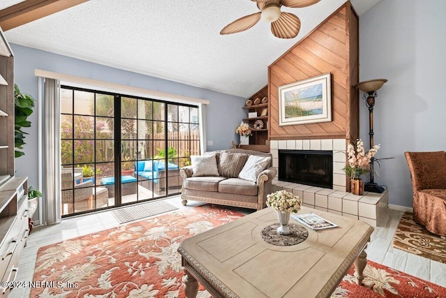 living room with light hardwood / wood-style flooring, vaulted ceiling, a tile fireplace, and a textured ceiling