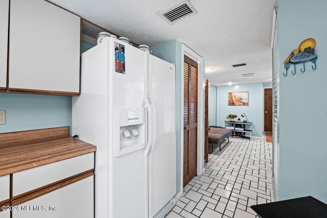 kitchen with a textured ceiling, white refrigerator with ice dispenser, and white cabinets