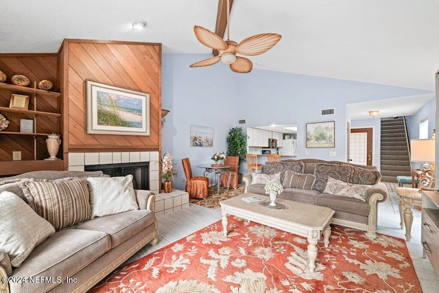 living room with built in features, high vaulted ceiling, a tiled fireplace, ceiling fan, and light hardwood / wood-style floors