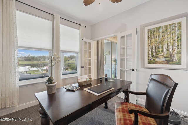 carpeted office space featuring a healthy amount of sunlight, ceiling fan, and a water view