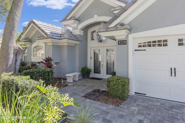 view of exterior entry with a tiled roof, french doors, a garage, and stucco siding