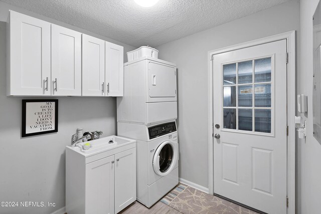 washroom with light wood-type flooring, a textured ceiling, cabinets, and stacked washer and clothes dryer