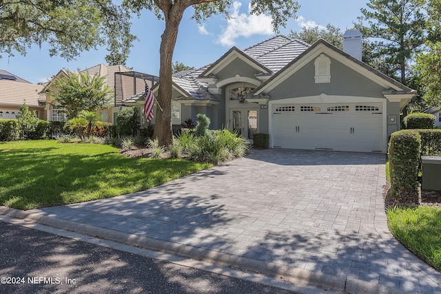 view of front of property featuring stucco siding, a front lawn, decorative driveway, an attached garage, and a chimney