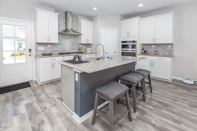 kitchen featuring gas cooktop, a sink, double oven, a kitchen breakfast bar, and wall chimney exhaust hood