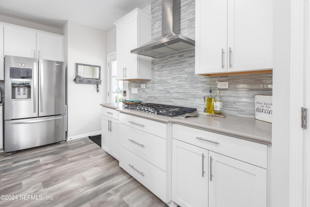 kitchen featuring white cabinetry, stainless steel appliances, wall chimney exhaust hood, light countertops, and decorative backsplash