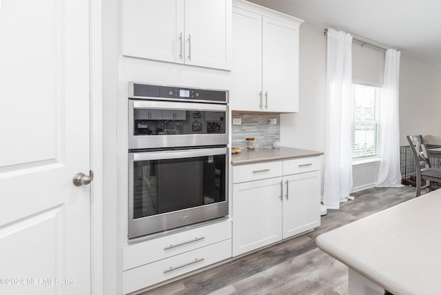 kitchen featuring double oven, light countertops, decorative backsplash, light wood-style floors, and white cabinets