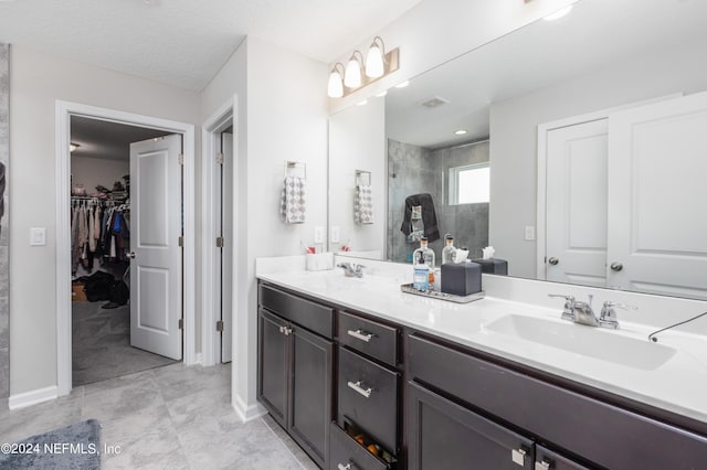 bathroom featuring double vanity, a spacious closet, tiled shower, and a sink