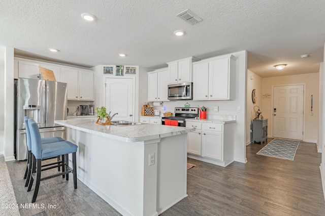 kitchen with dark wood-style floors, appliances with stainless steel finishes, white cabinets, a sink, and an island with sink