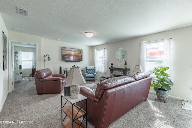 carpeted living area featuring a textured ceiling, a stone fireplace, visible vents, and baseboards