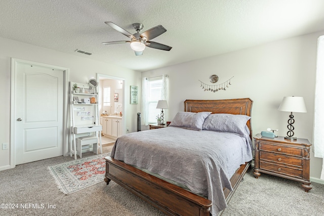 bedroom with a textured ceiling, ensuite bath, carpet flooring, and visible vents