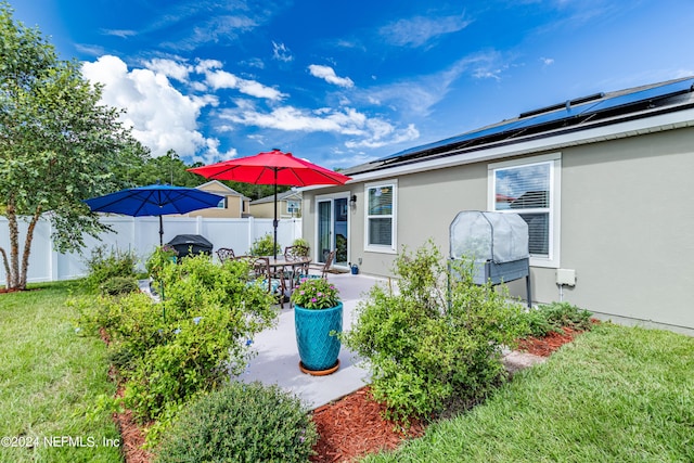 rear view of property with a lawn, a patio, a fenced backyard, roof mounted solar panels, and stucco siding