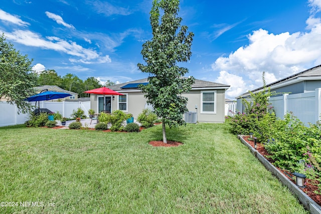 rear view of property featuring a yard, a patio area, a fenced backyard, and roof mounted solar panels