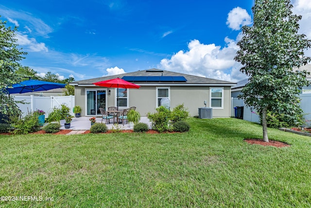 back of house featuring solar panels, a lawn, a patio, fence, and stucco siding