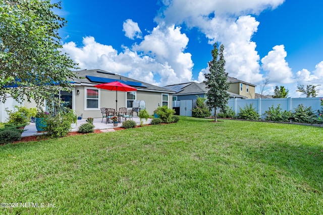 rear view of property with a yard, a patio, solar panels, stucco siding, and fence