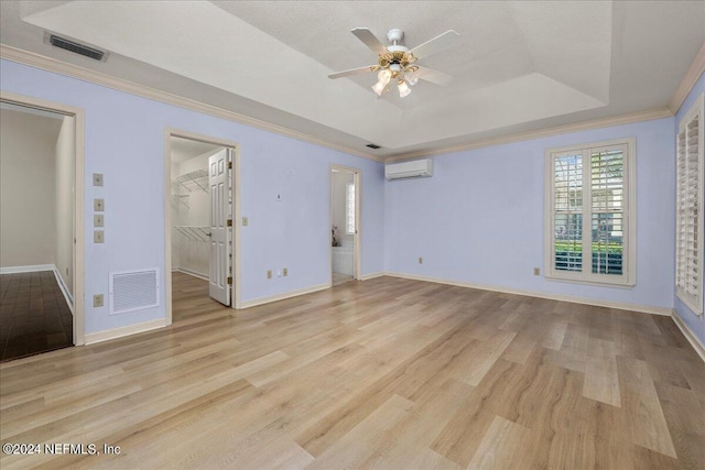 spare room with light wood-style flooring, a wall unit AC, a raised ceiling, and visible vents