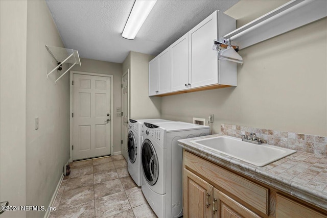 laundry room with a textured ceiling, separate washer and dryer, a sink, baseboards, and cabinet space