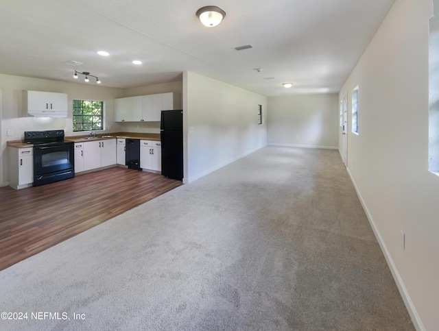 kitchen featuring dark colored carpet, a sink, white cabinets, open floor plan, and black appliances