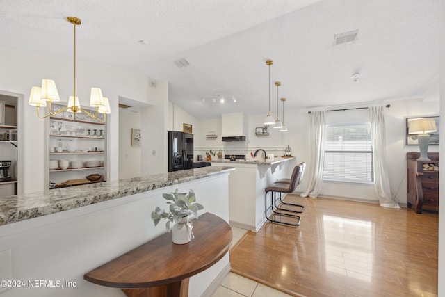 kitchen with white cabinets, light hardwood / wood-style floors, a textured ceiling, black refrigerator with ice dispenser, and vaulted ceiling