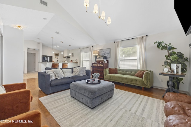 living room with a notable chandelier, vaulted ceiling, and light hardwood / wood-style floors