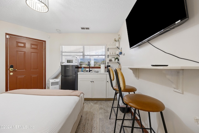 bedroom featuring refrigerator, a textured ceiling, light hardwood / wood-style flooring, and sink