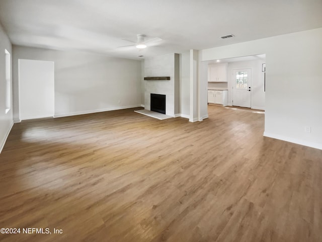 unfurnished living room with light wood finished floors, visible vents, a large fireplace, ceiling fan, and baseboards