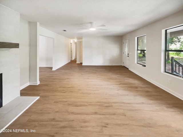 unfurnished living room featuring light wood-style flooring, visible vents, baseboards, a ceiling fan, and a tiled fireplace