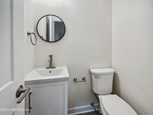 half bath with toilet, baseboards, and vanity